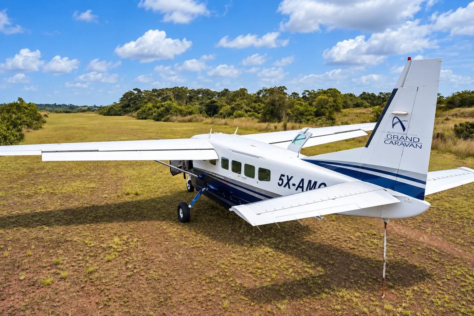 Asante Aviation Grand Caravan 5X-AMC parked on a remote grass airstrip, showing the Asante tail logo